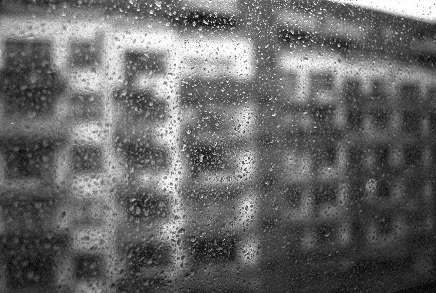 Raindrops cover a window with a blurry building visible in the background.