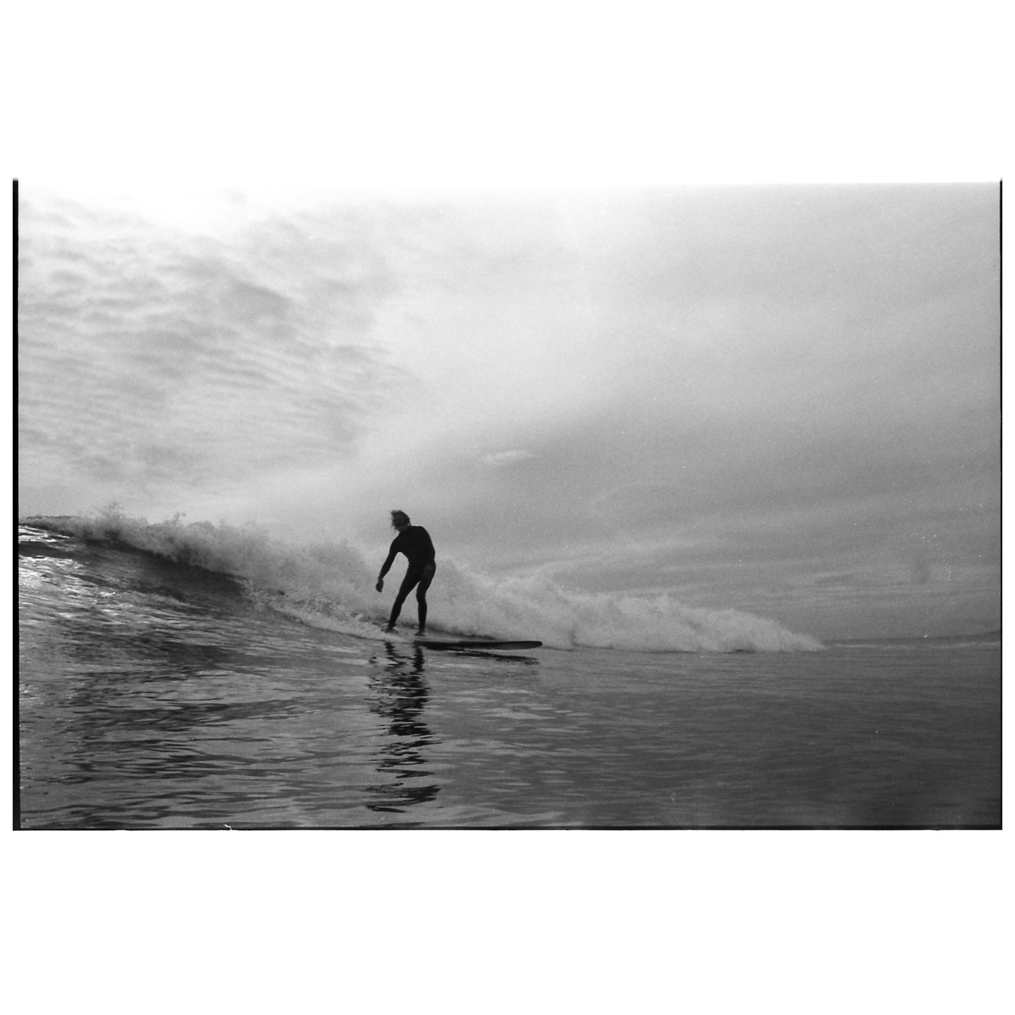 A surfer rides a wave on a cloudy day.