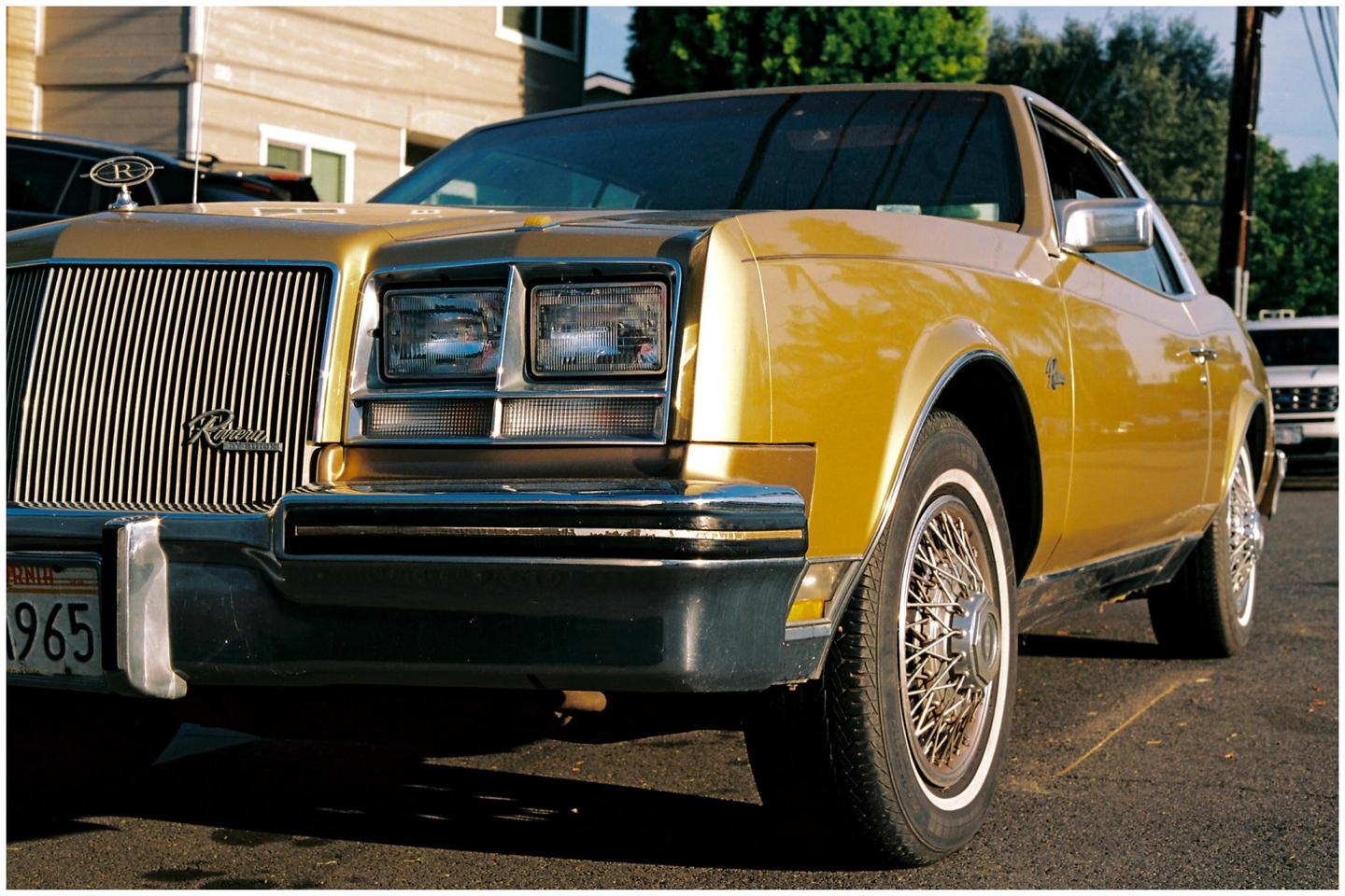 A gold car with a prominent grille and headlights is parked on a street.