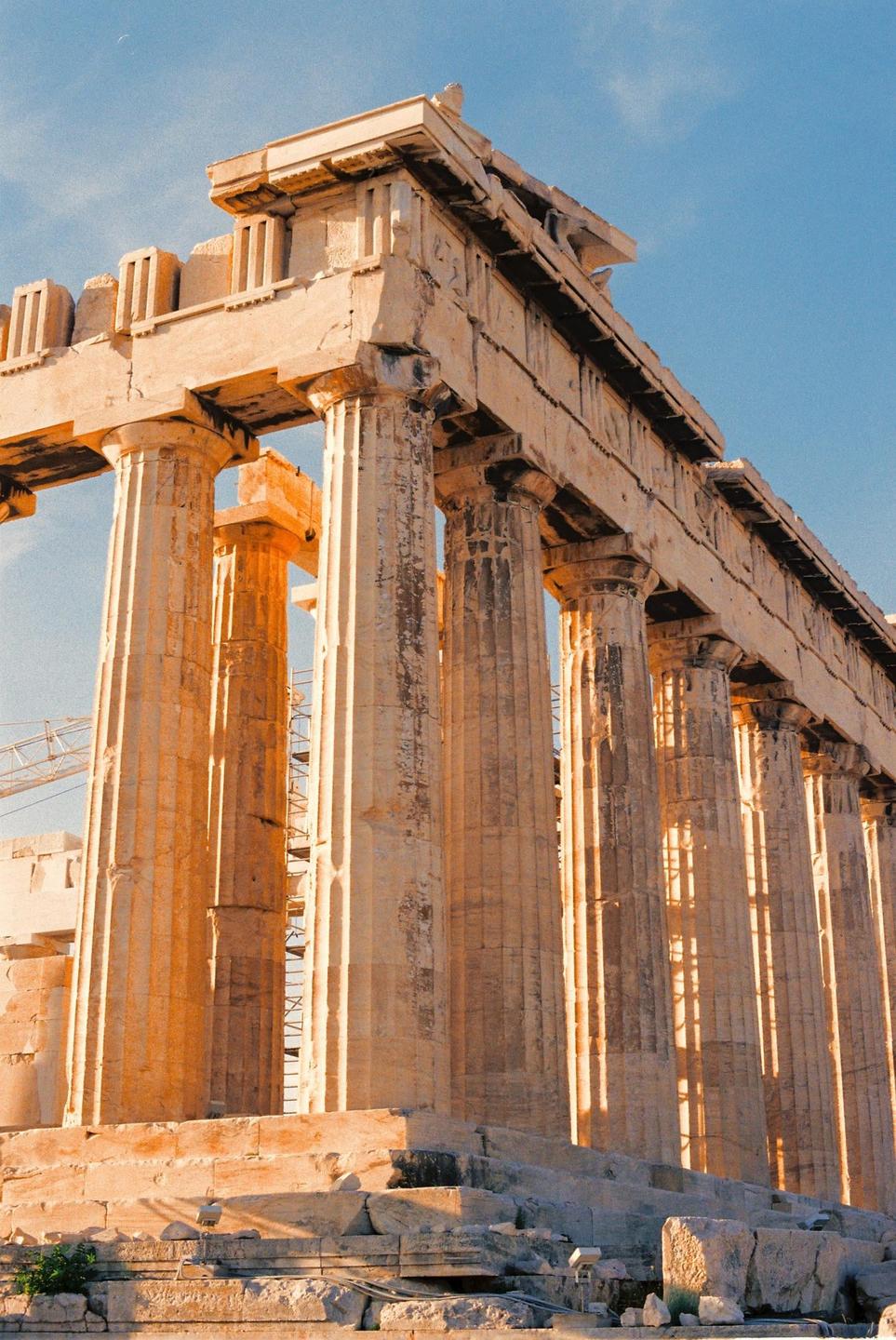 The Parthenon is illuminated by golden hour light against a clear blue sky.