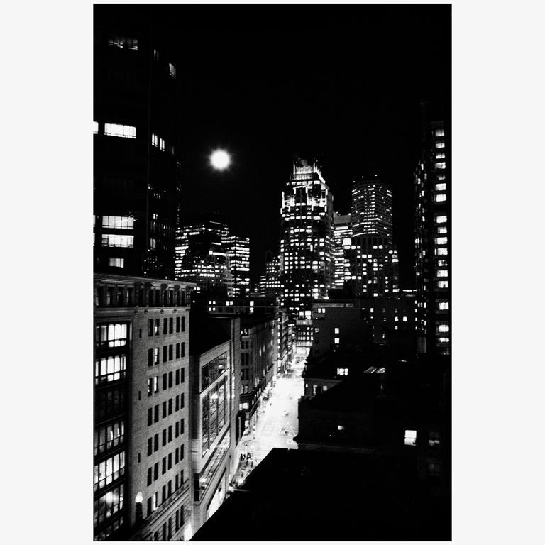 A full moon illuminates a city street lined with buildings at night.