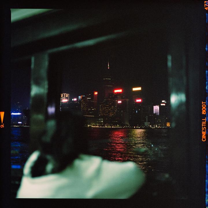 A person on a ferry looks out at the illuminated skyline of Hong Kong at night.