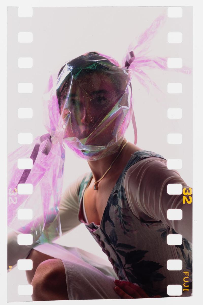 A woman with a shiny pink plastic bag over her head is wearing a floral top and a necklace.