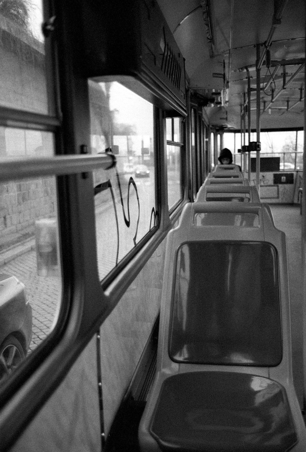 A person sits alone in a bus with empty seats, looking out the window at a street.