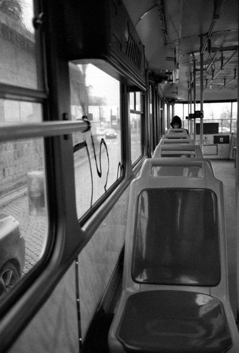A person sits alone in a bus with empty seats, looking out the window at a street.