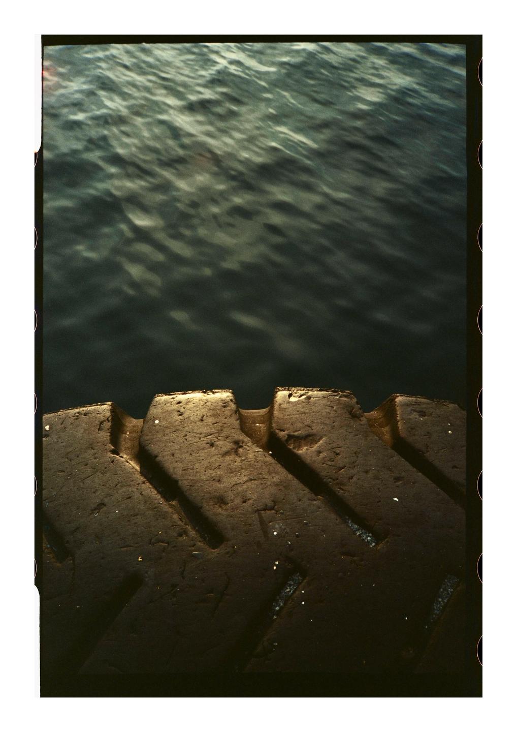 A close-up of a tire tread is visible in the foreground with rippling water in the background.