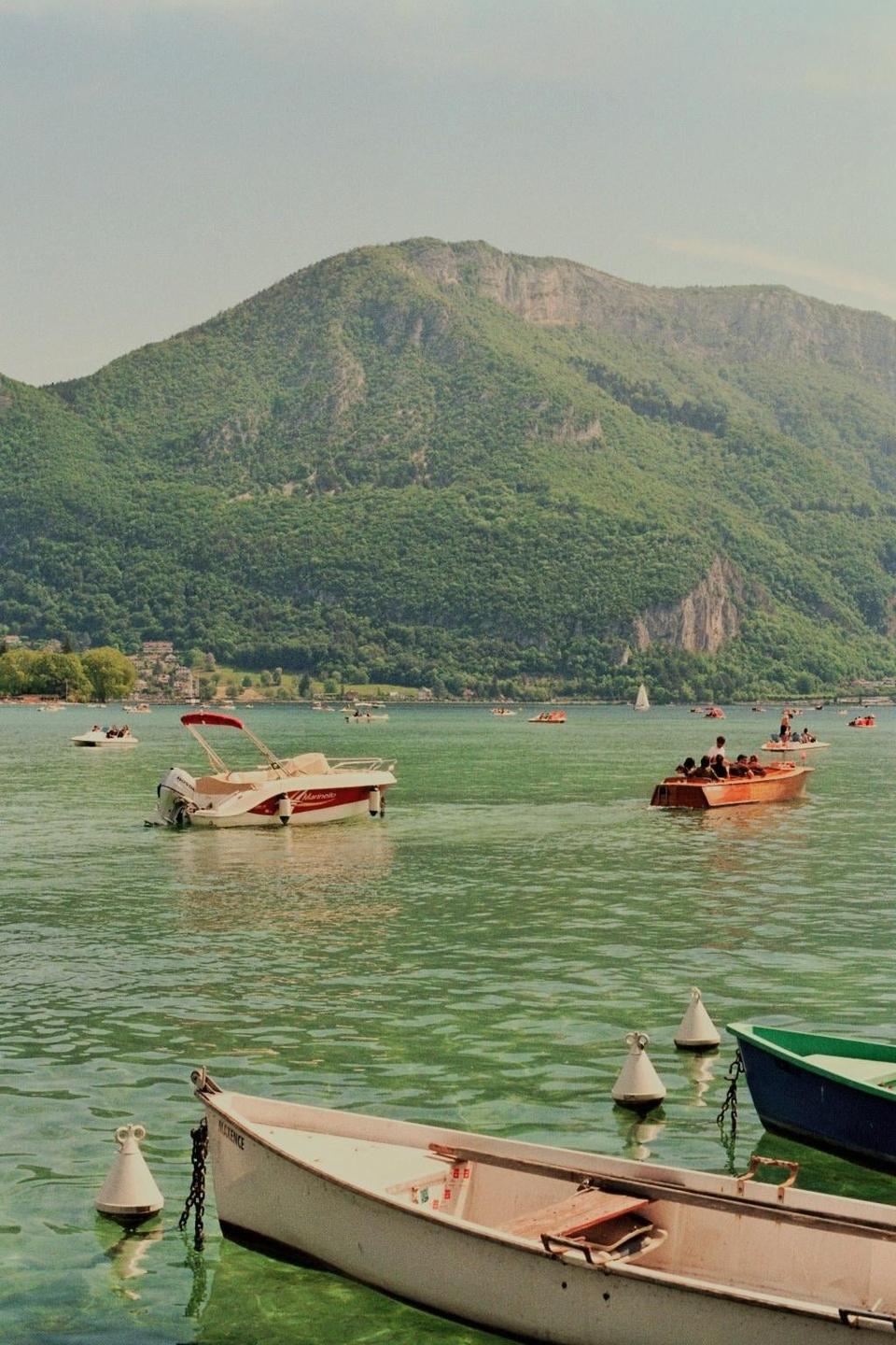 Several boats are on a lake with a large, tree-covered mountain in the background.
