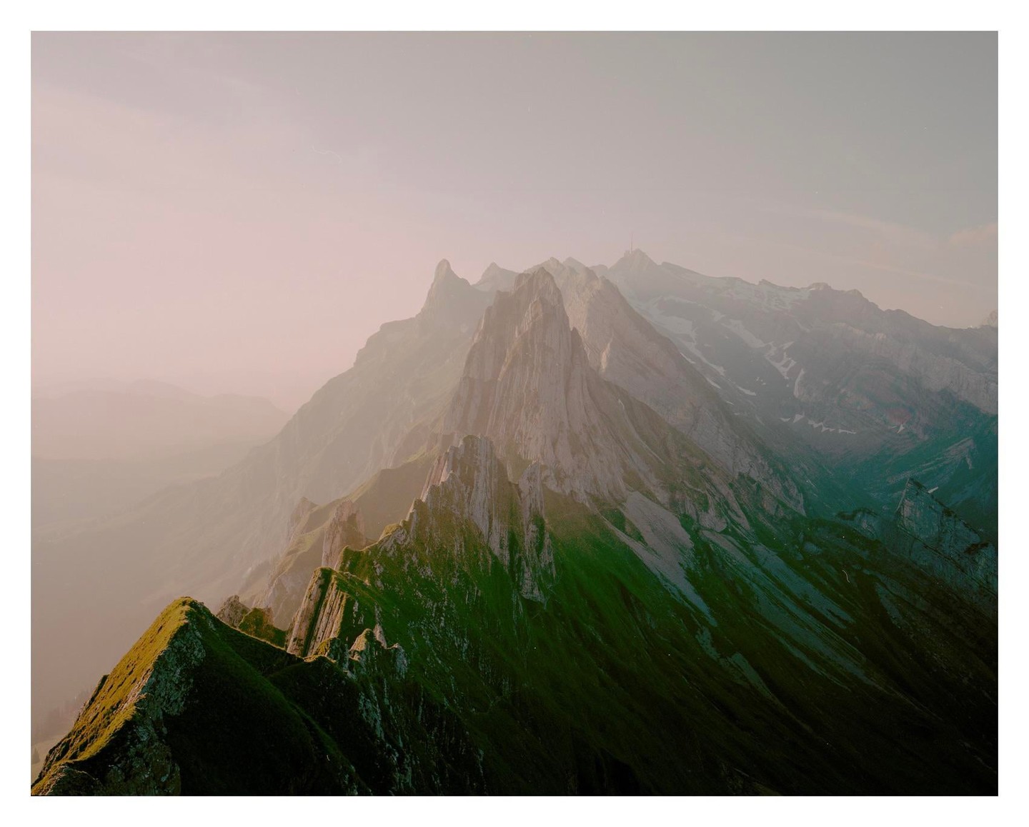 Sunlight illuminates the ridges of a mountain range with hazy peaks in the distance.