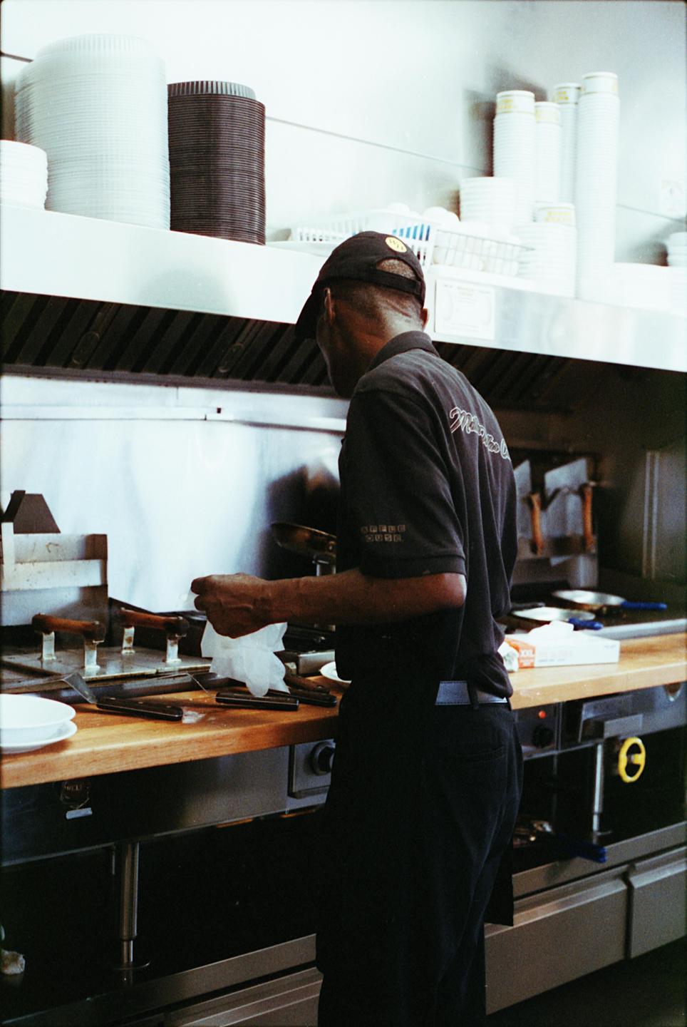 A man in a black shirt and cap is working in a commercial kitchen.