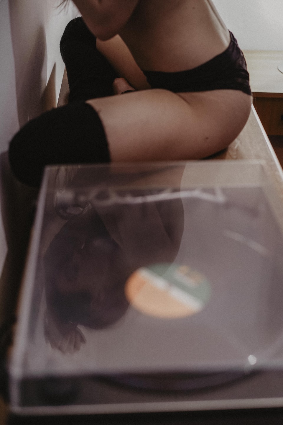 A woman sits on a wooden surface with a record player in the foreground.