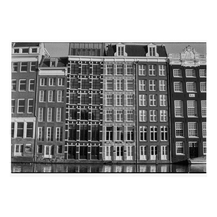 A row of tall, narrow buildings with many windows stands along a canal.