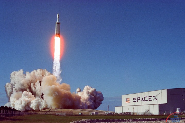 A SpaceX Falcon Heavy rocket launches into a clear blue sky, leaving a trail of fire and smoke.