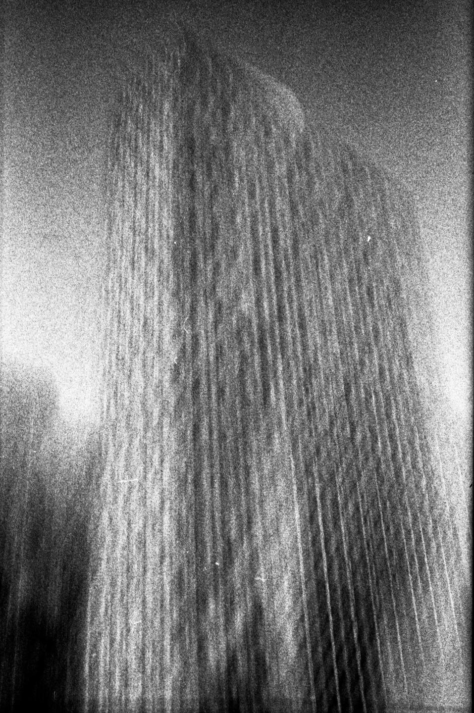 A blurry, grainy black and white image shows a tall, dark, textured structure with vertical lines.