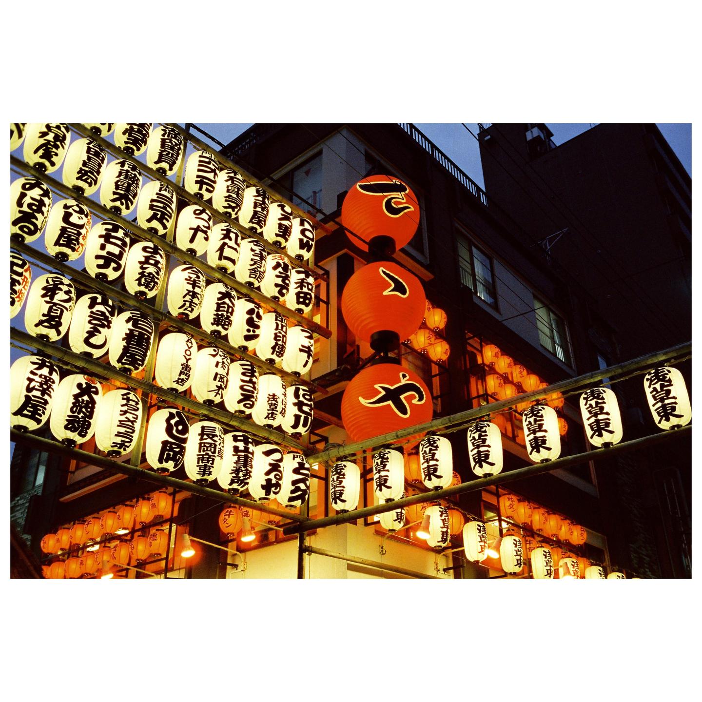 Many lanterns with Japanese writing hang from a building at night.