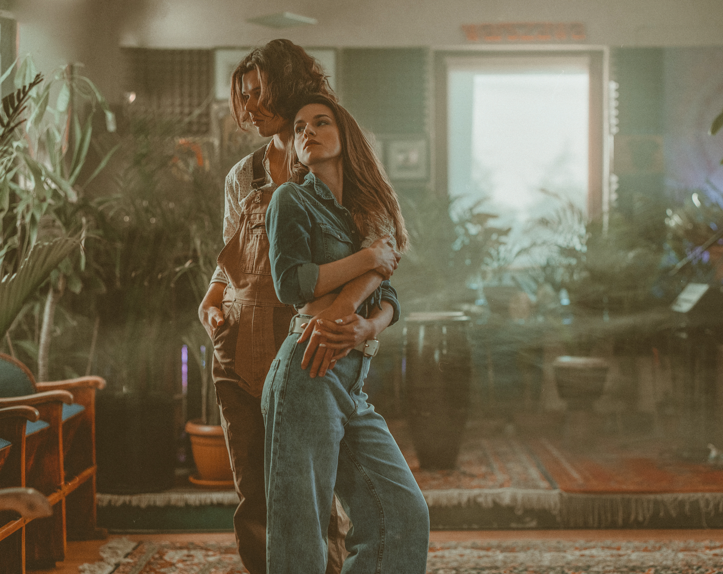 A couple embraces in a room filled with plants and a patterned rug.