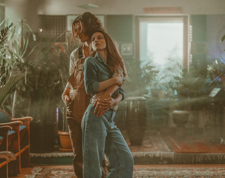 A couple embraces in a room filled with plants and a patterned rug.