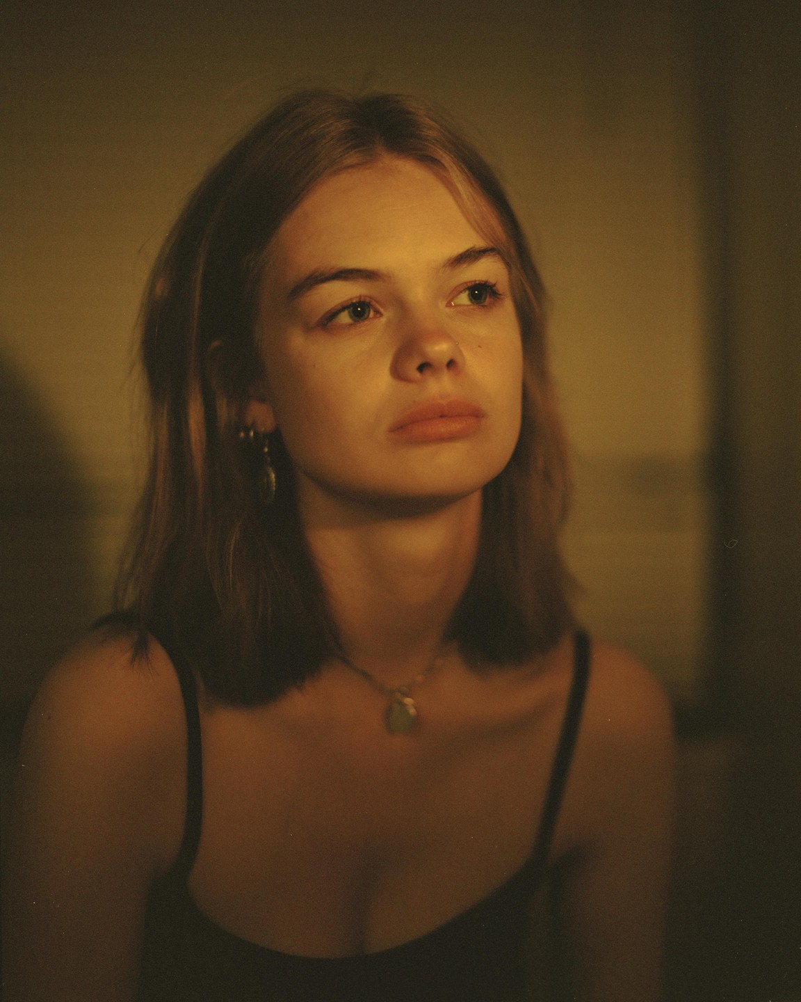 A woman with light brown hair and a necklace looks up and to the right.