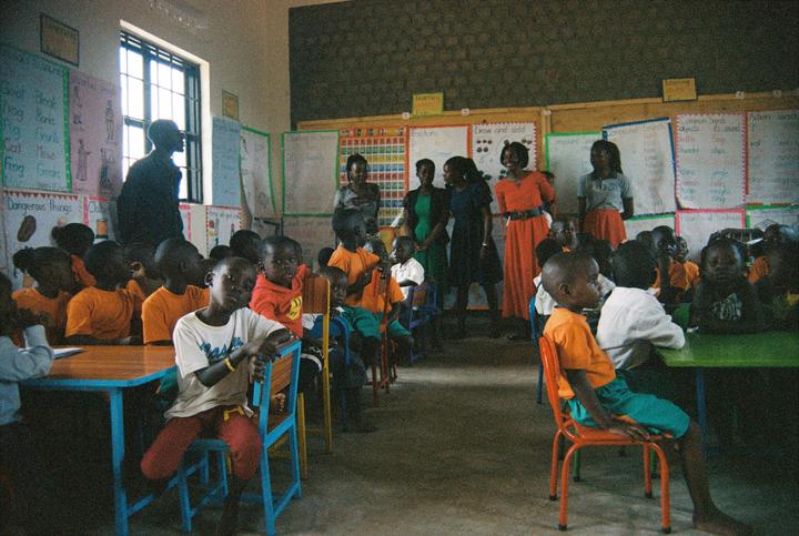 A group of children and adults are gathered in a classroom with educational posters on the walls.