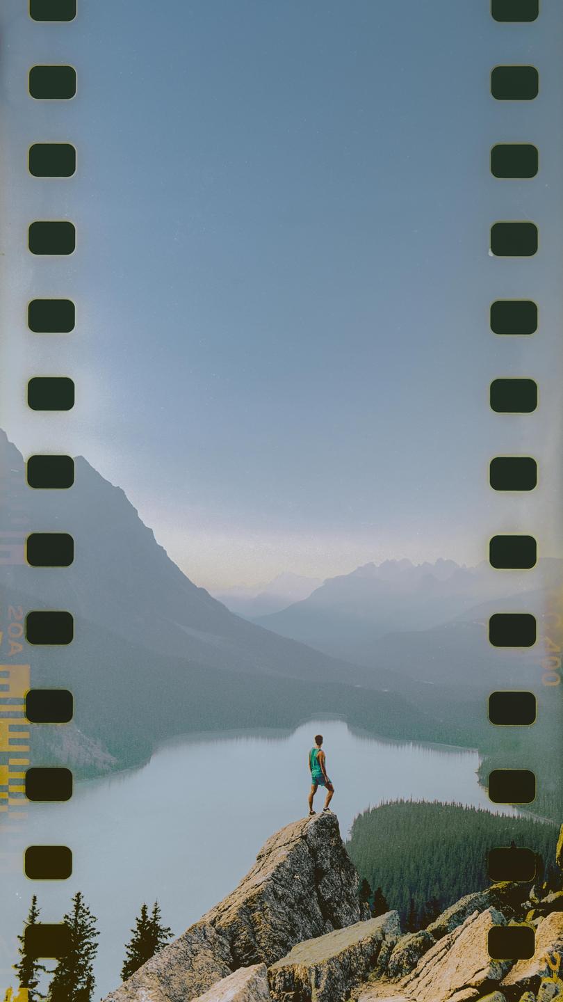 A man stands on a rocky peak overlooking a lake and mountains.