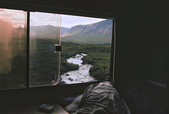 A view of a winding river and mountains from inside a vehicle with a blanket and a pack of cigarettes on a table.