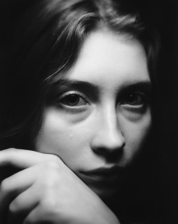 A woman with a tear on her cheek rests her chin on her hand.