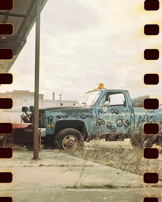A blue pickup truck with graffiti on its side is parked in a grassy area next to a building.