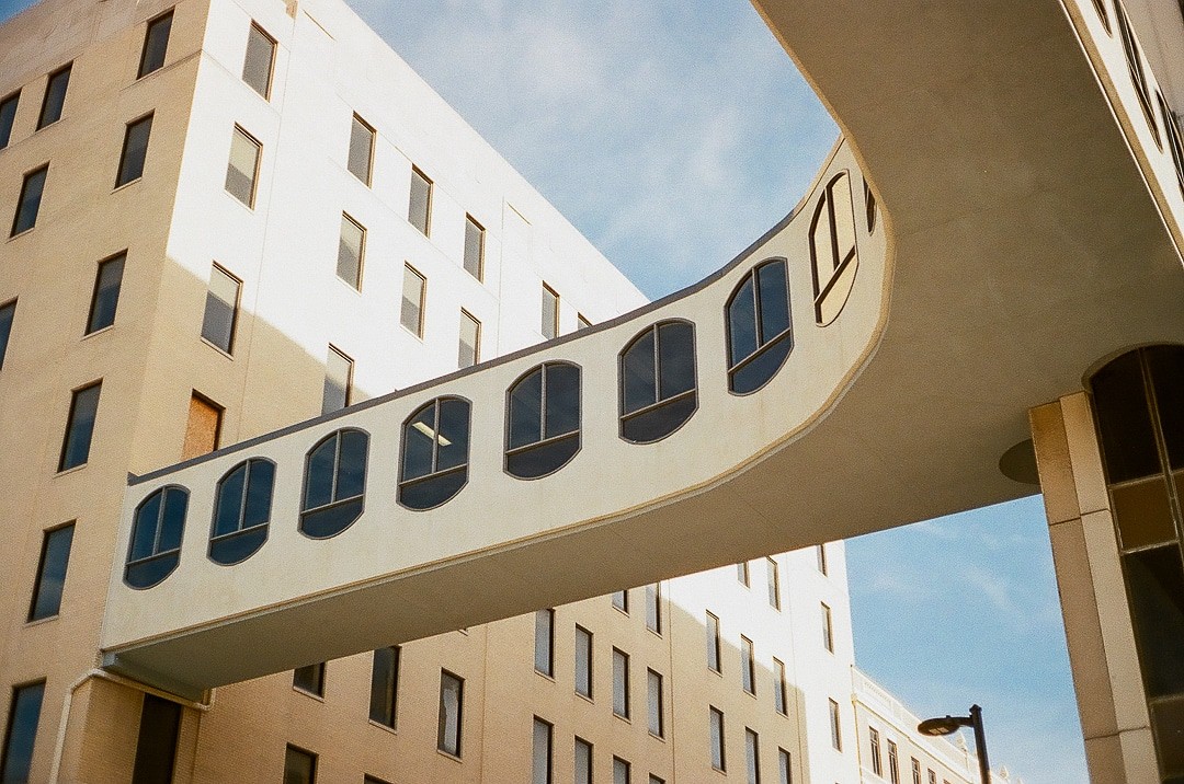 A curved skywalk with arched windows connects two buildings under a blue sky.