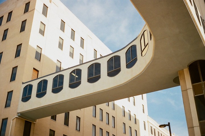 A curved skywalk with arched windows connects two buildings under a blue sky.
