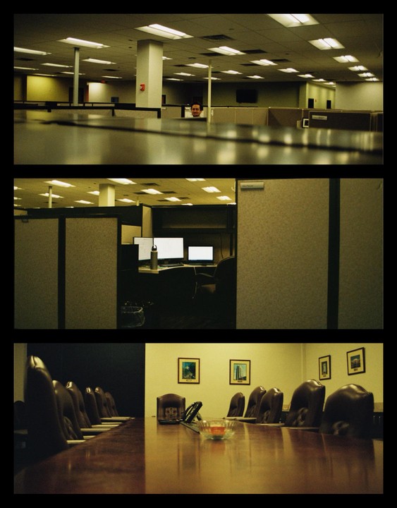 A man peeks over a cubicle in an office with a conference room and another cubicle visible below.