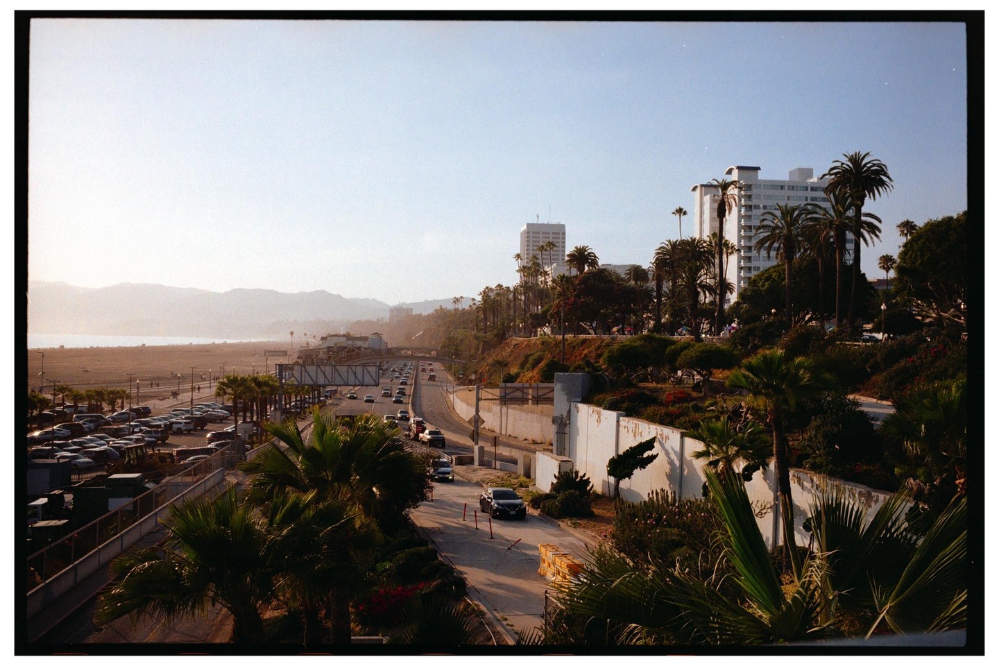 A wide view shows a highway with cars, a beach, and buildings with palm trees under a clear sky.