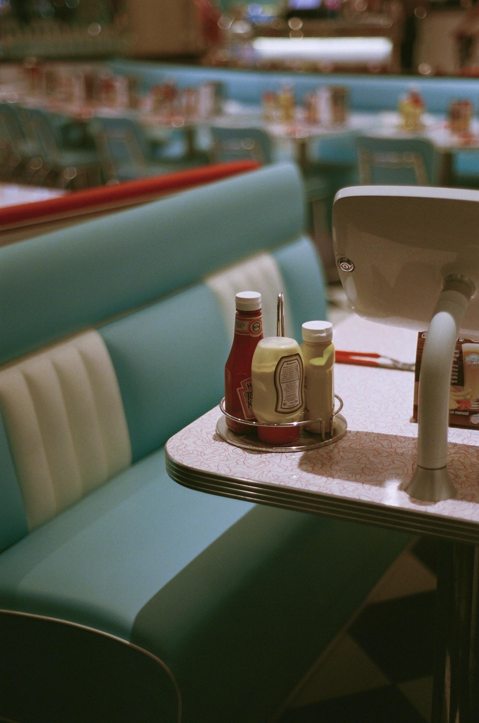A diner booth with a table holding condiments and a menu is shown with other booths blurred in the background.