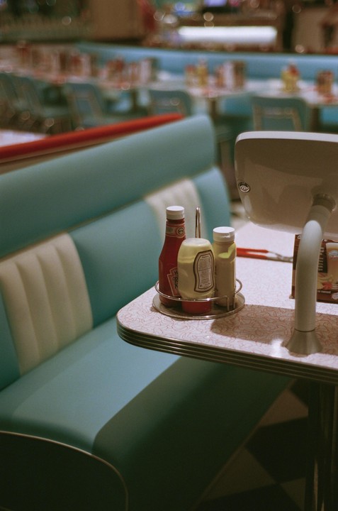 A diner booth with a table holding condiments and a menu is shown with other booths blurred in the background.