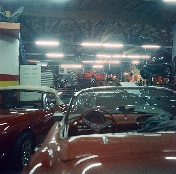 Several vintage cars are parked inside a garage with some cars on lifts.