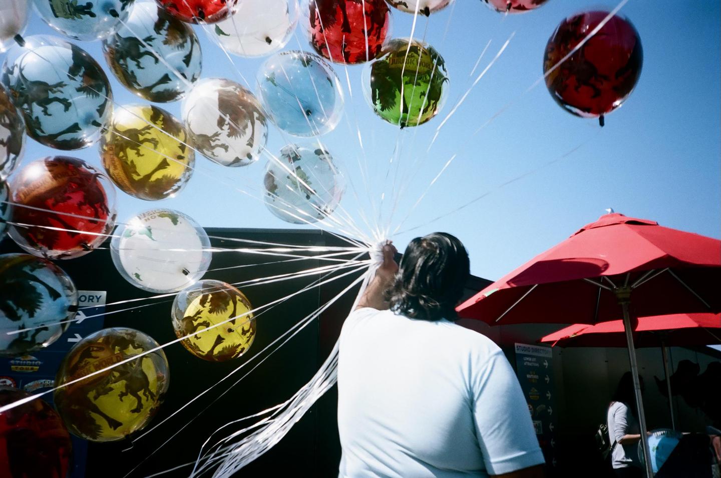 A person holds a large bunch of dinosaur-themed balloons under a clear blue sky at Universal Studios.
