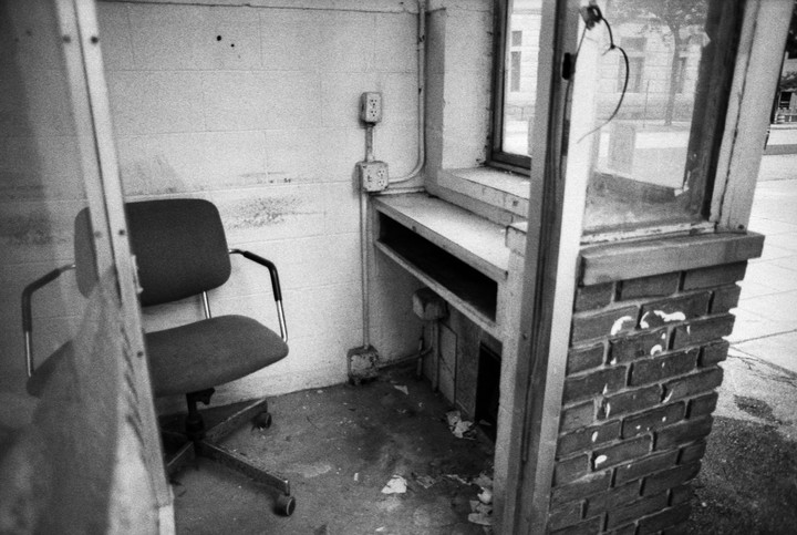 An empty office chair sits inside a small, dilapidated booth with a window looking out onto a street.
