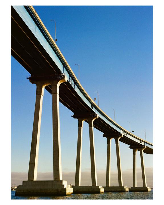 A long bridge with many pillars extends over water under a clear blue sky.