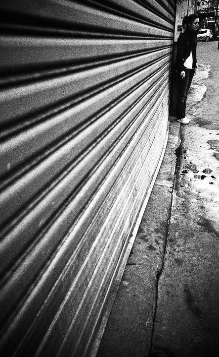 A woman stands next to a corrugated metal wall on a street.