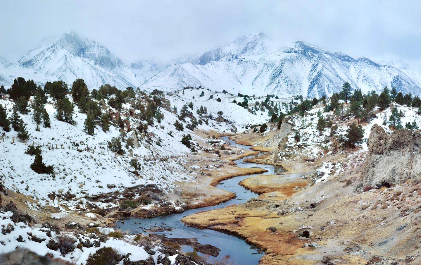 A winding river flows through a snowy valley with mountains in the background.