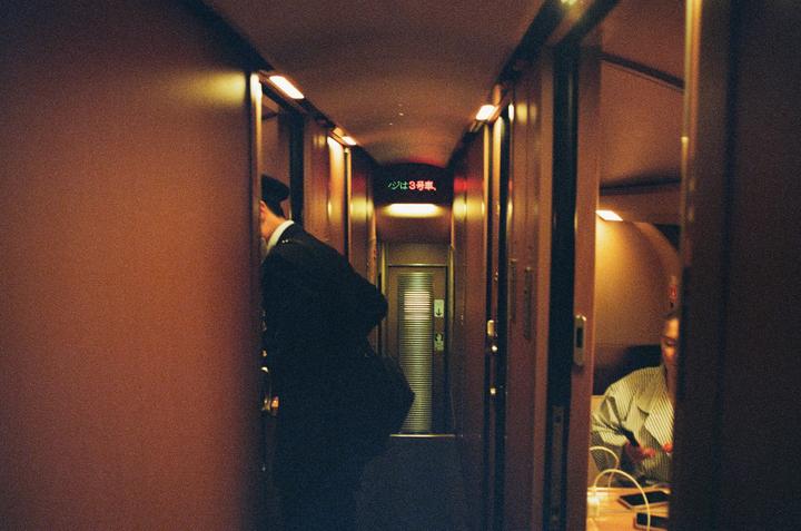 A man in uniform walks down a narrow corridor with a red illuminated sign in Japanese.