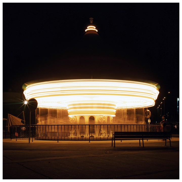 A brightly lit carousel spins at night, creating light trails.