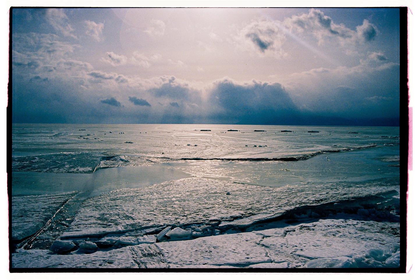 A vast expanse of frozen water with broken ice sheets stretches under a cloudy sky.