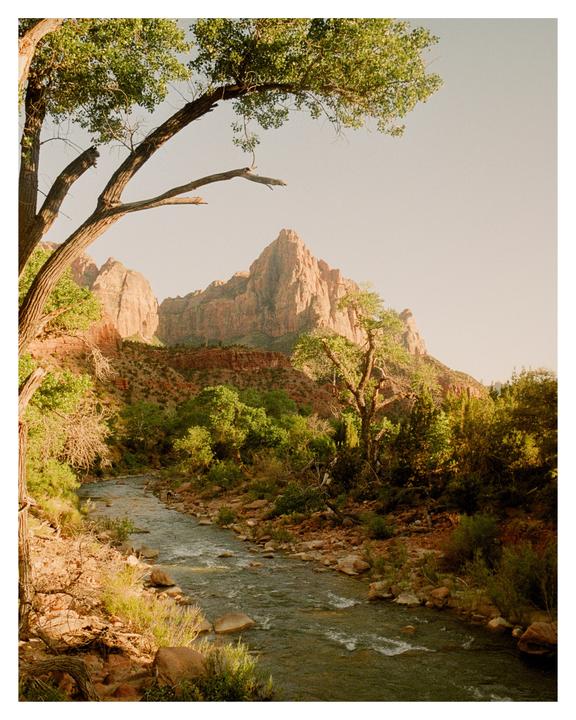A river flows through a valley with trees and mountains under a clear sky.