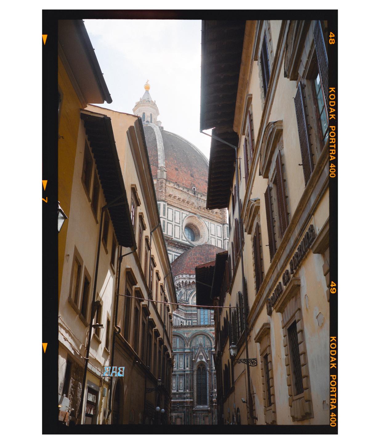 A narrow street leads to a large domed building in a city.