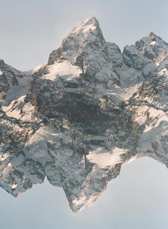 A double exposure shows a snow-covered mountain peak reflected upside down against a clear sky.