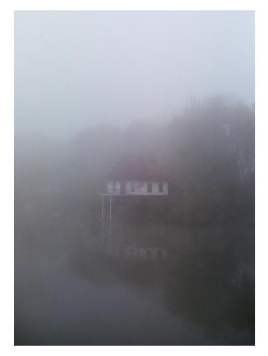 A house with a red roof is partially visible through a thick fog.