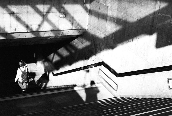 A person with a backpack walks down a set of stairs with strong shadows cast on the walls and steps.