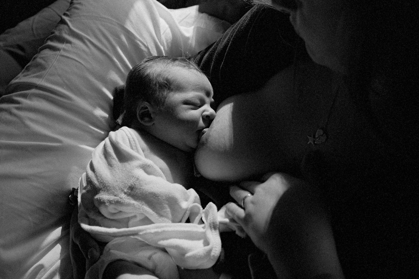 A newborn baby is breastfeeding while being held by a woman.