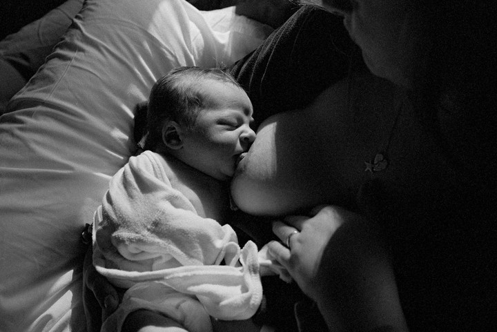 A newborn baby is breastfeeding while being held by a woman.