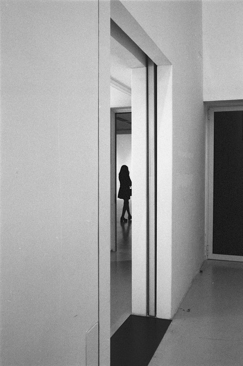A woman stands silhouetted in a doorway, looking down a hallway.