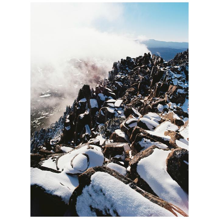 Snow covers the rocky summit of a mountain with clouds partially obscuring the view.